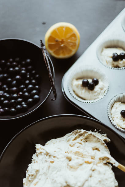 Muffin dough and filled molds and a bowl filled with blueberries and a spoon