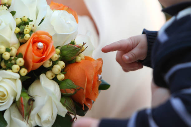 Small child points at a bridal bouquet filled with orange and white roses