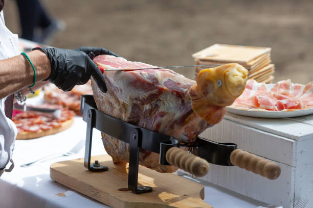 Chef wearing black gloves slicing prosciutto ham from a leg on a stand at an outdoor event