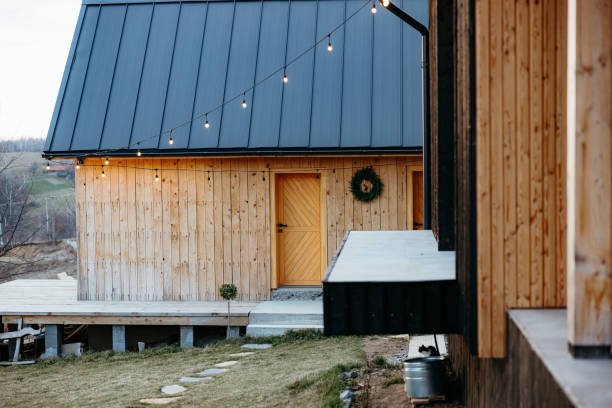 Modern wooden cabin with a porch and string lights is bathed in the warm glow of the setting sun
