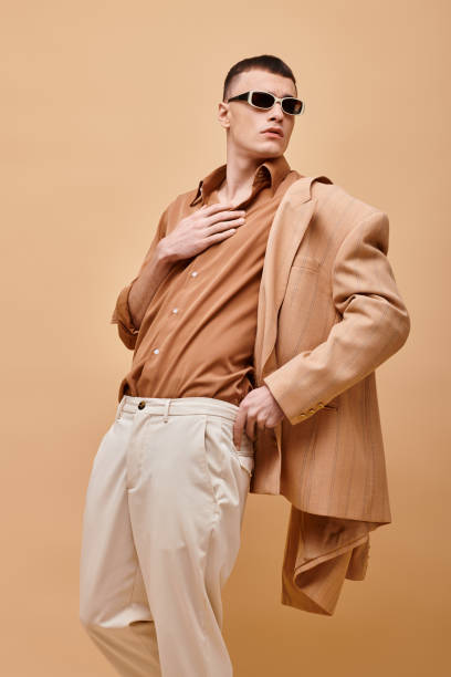 istock A stylish man confidently posing against a vibrant orange backdrop in a chic outfit 2173112695