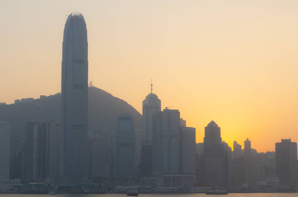 One of Hong Kong's iconic ferries passes the terminal at Tsim Sha Tsui, on its way across the busy waters of Victoria Harbour. In the distance, silhouetted against the setting sun, are the towering skyscrapers of Hong Kong Island.
