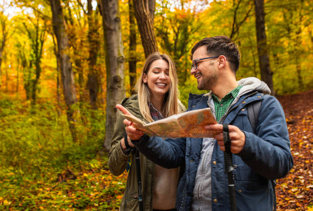 istock Smiling couple with backpacks hiking together in forest using map for direction. 2173128254