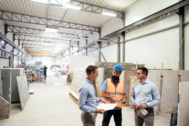 Employees in modern factory or warehouse working together. Manager talking to shift manager wearing protective helmet and uniform Employees working in modern factory with automated machines and robots for efficient production cad drawing services stock pictures, royalty-free photos & images