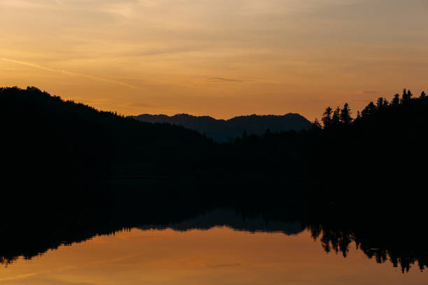 istock A tranquil sunset over a calm lake, with silhouetted mountains and trees reflected perfectly in the water 2173141549