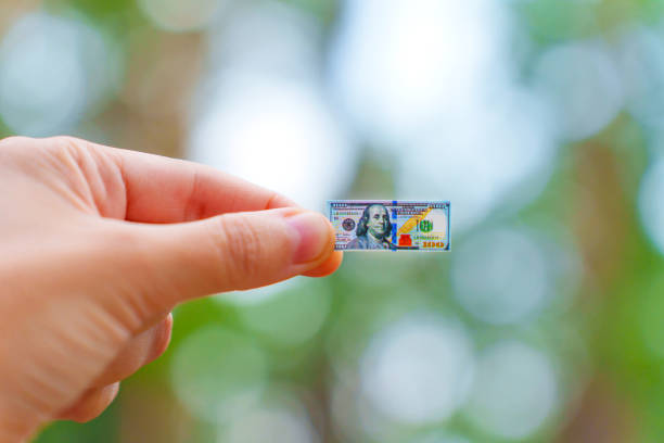 A hand holding a tiny hundred dollar bill against a vibrant bokeh background, representing unique financial concepts and aspirations.
