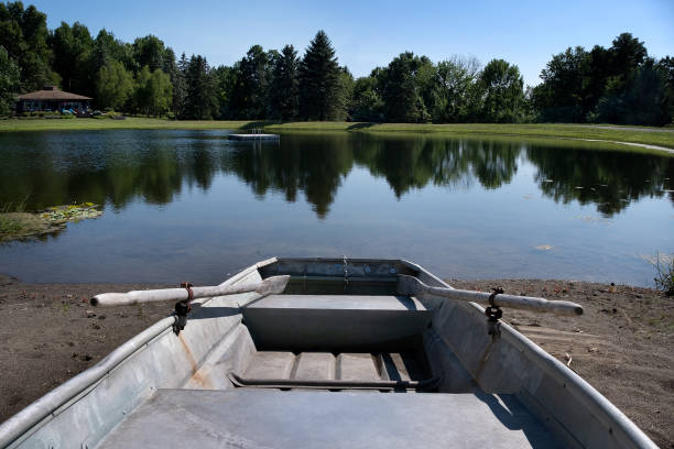 Small blue rowboat floating on a calm park pond, surrounded by greenery and reflecting in the water.