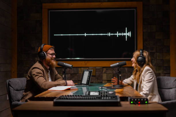 istock Two radio hosts talking and smiling while sitting near microphones in broadcasting studio 2173154163