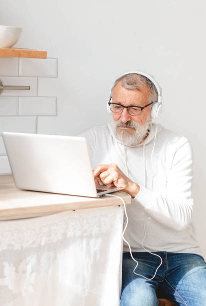 istock Portrait handsome old man dressed in hoodie and eyeglasses is using laptop and smiling while listen music sitting on couch at home 2173191805