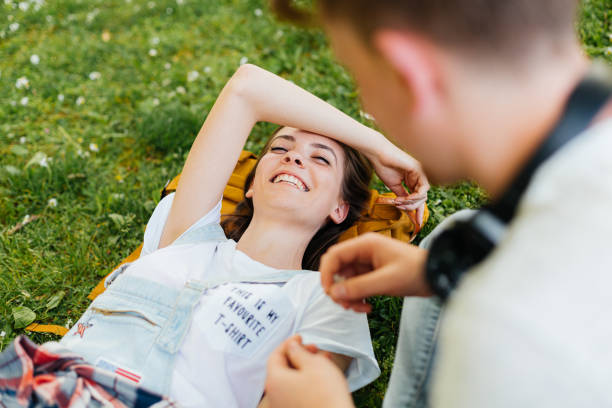 Young people male and female lying on the grass smiling and talking, hanging out together outdoors