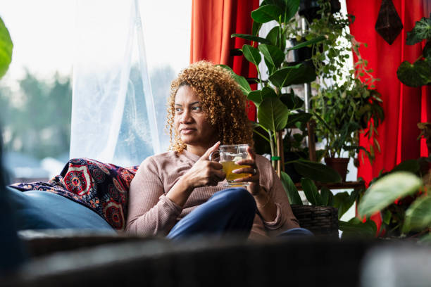 istock Multiracial woman at home on sofa drinking tea, thinking 2173201519