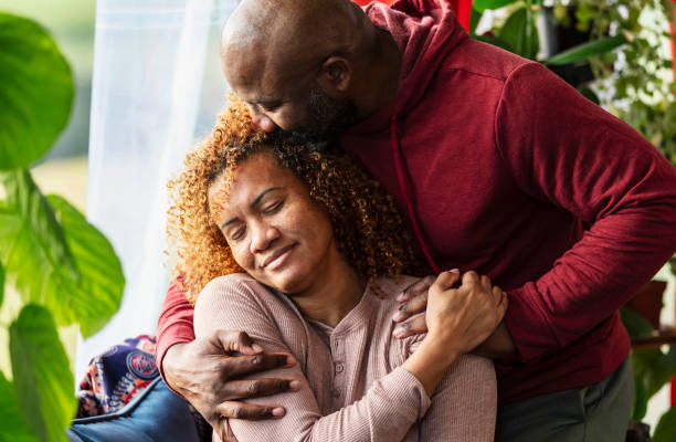 Affectionate mature couple, man hugging wife, at home A mature man shows his wife how much he love her, wrapping his arms around her shoulders to give her a hug, and kissing her on the side of her head. She is smiling with her eyes closed, resting her hand on his. shaved black women stock pictures, royalty-free photos & images