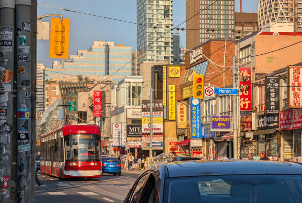 Toronto, Canada - August 25, 2024: The TTC Dundas streetcar heads west on Dundas Street West at Huron Street. Multilingual retail signs line this route in the Kensington-Chinatown neighbourhood.