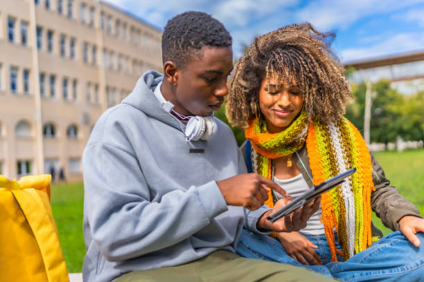 istock Smiling multiethnic couple using tablet sitting outside the university campus 2173208890