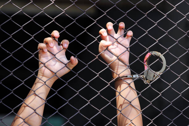 istock Hands Grasping a Chain Link Fence Behind Bars 2173242605