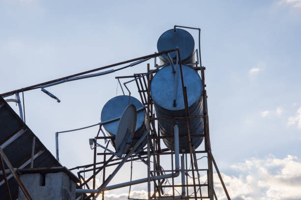 A view of metal water tanks and satellite dishes on a rooftop. The image shows pipes, structures, and equipment used in urban water management under a bright sky.