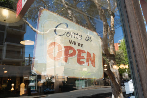 Come in, we're open sign behind glass with street reflections.