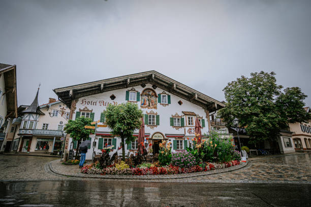 Oberammergau, Germany - September 14, 2024 - A picturesque hotel with murals and colorful flowerbeds in a quaint European town, captured on a rainy day, showcasing traditional Bavarian architecture.