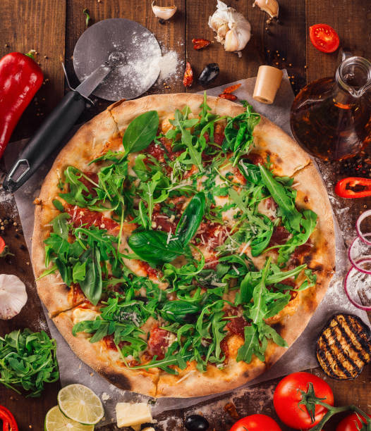 Delicious pizza with fresh arugula lying on wooden table surrounded by ingredients