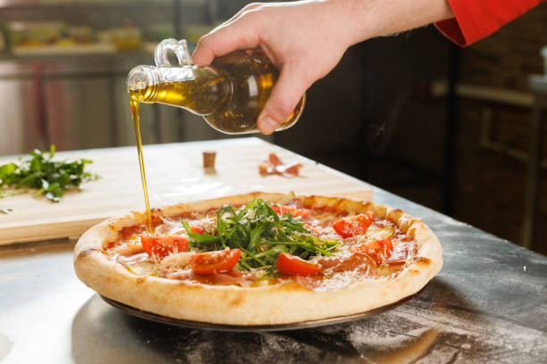 istock Pouring olive oil on freshly baked pizza with arugula and tomatoes 2173280556