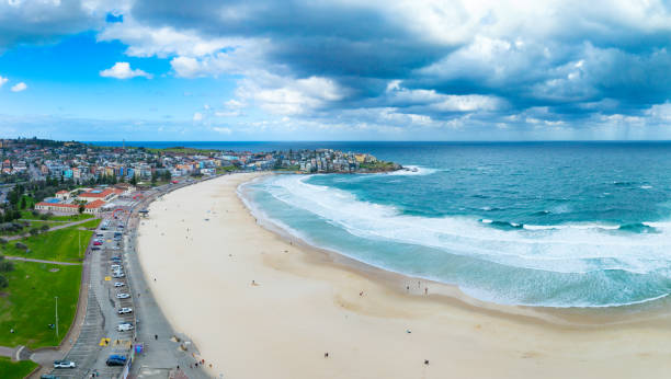 Capture the essence of summer with an aerial view of people relaxing on Bondi Beach, Sydney, under a dramatic afternoon sky, enjoying the sun and surf.