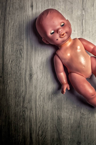 Creepy vintage doll lies on a gray wooden floor, evoking childhood nostalgia and loneliness with a haunting atmosphere