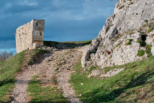 An image of a dirt path leading uphill towards an old stone structure, surrounded by rocky terrain and patches of greenery. Vitoriano, Araba, Basque Country, Spain.