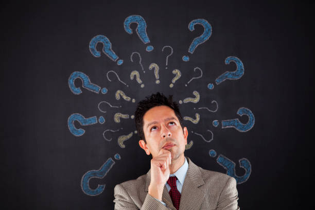 istock a man with a suit and tie is looking up at a blackboard with question marks on it 2173314954