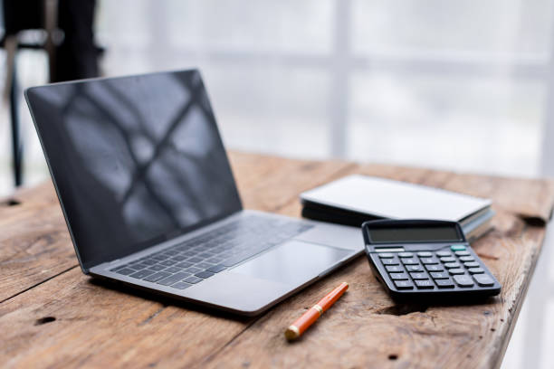 istock Laptop Computer, notebook, and eyeglasses sitting on a desk in a large open plan office space after working hours 2173320905