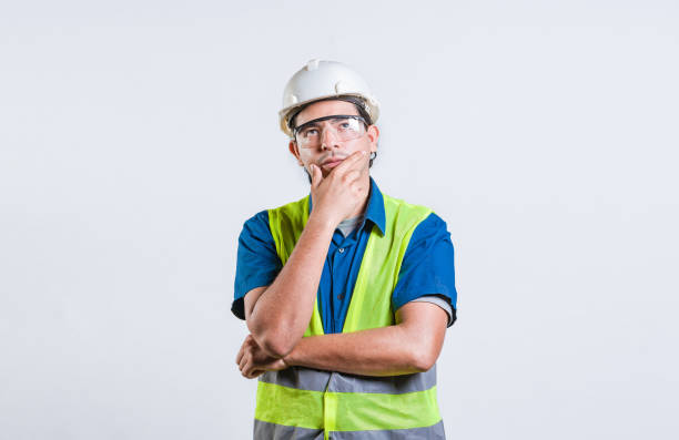 istock Young builder wondering looking up with hand on chin. Pensive builder man with hand on chin isolated 2173335607