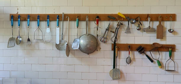 Old cooking utensils hanging on tiled kitchen wall.