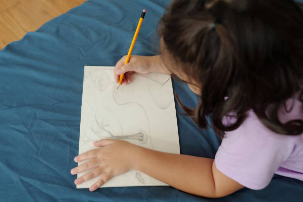 Close up little girl with blue pencil in hand sitting at the table and drawing stock photo