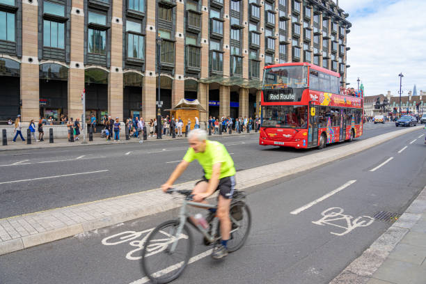 Red double-decker bus heading to Red Route, London.Individual riding a bicycle and people circulating on the public road