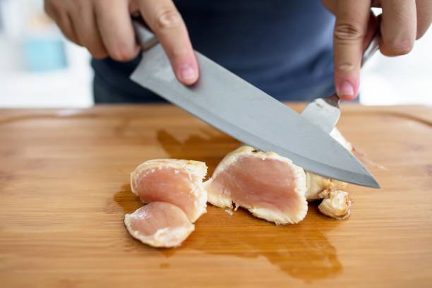 Slicing cooked chicken breast on a wooden cutting board