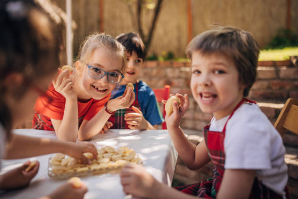An energetic group of children engage in outdoor baking, filled with cheerful glee, as they enthusiastically prepare dough together, highlighted by a sunny day ambiance.