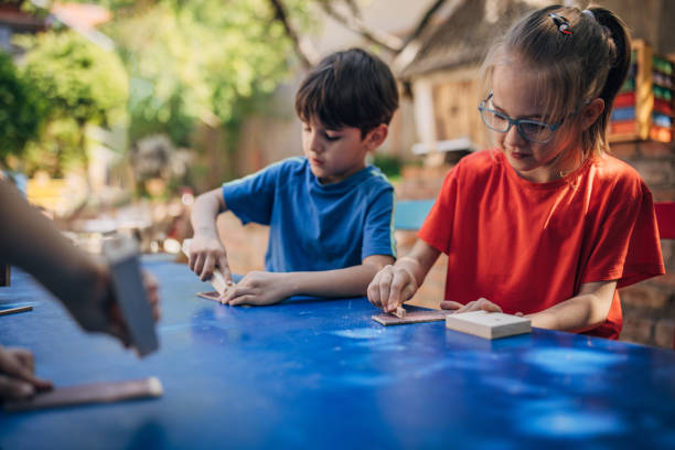istock Kids sanding wood blocks at outdoor blue table. 2173358781