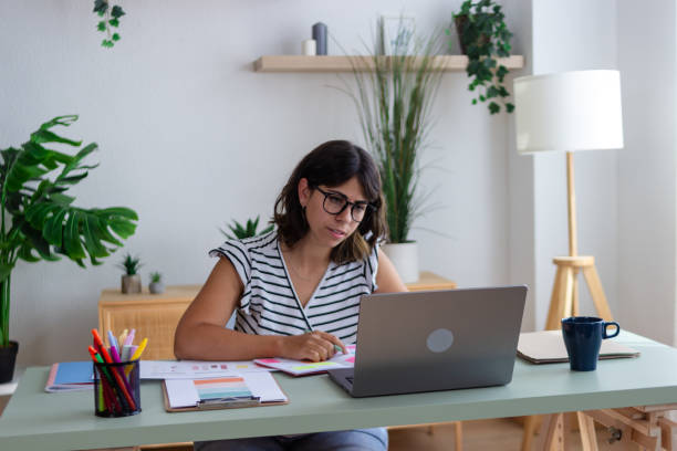 istock Focused young woman working from home office taking notes using laptop 2173362598