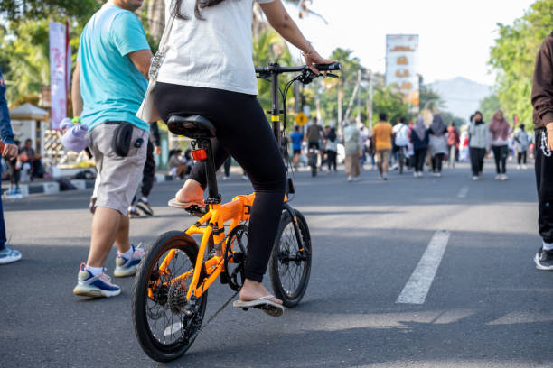 padang,indonesia-21 july 2024:A woman rides a bright orange folding bicycle through a busy street, surrounded by a blurred crowd of people.