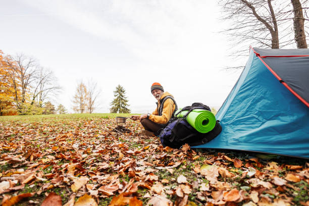 Mature man, hiker, backpacker, sitting on a ground by his tent preparing dinner