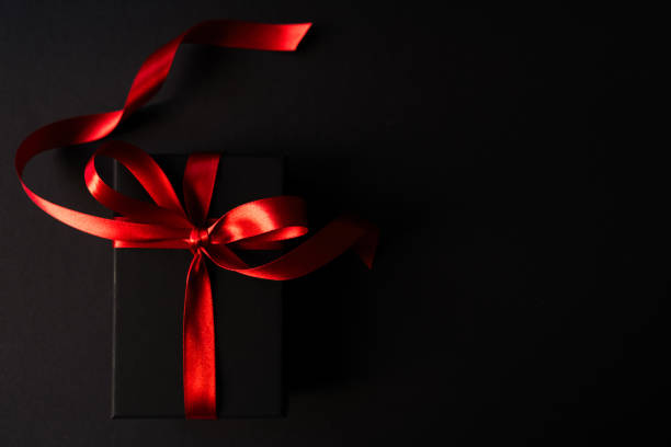istock Black box with red ribbon on the black background 2173383983