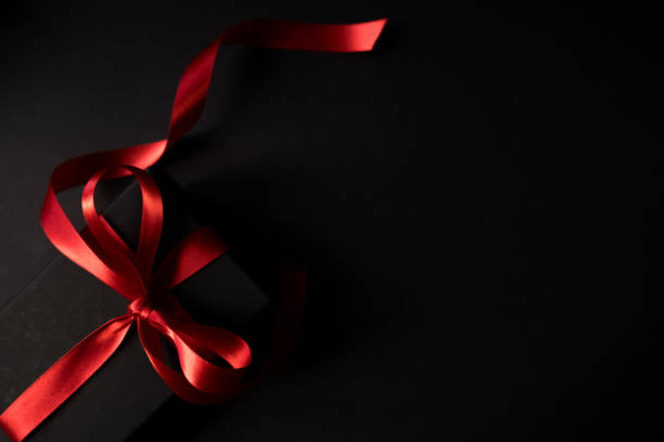 Black gift box with red ribbon on the black background