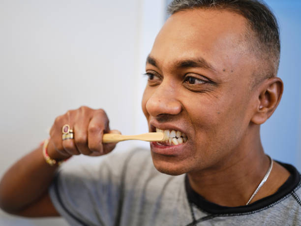 A mature Indian man looking in a bathroom mirror while brushing his teeth.