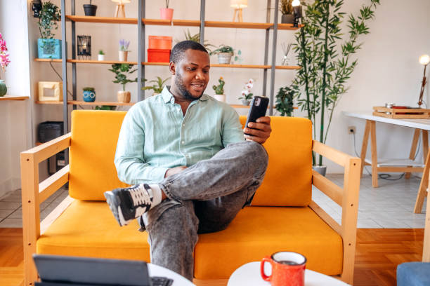 istock Young black man actively using mobile phone while resting in living room at home 2173398835