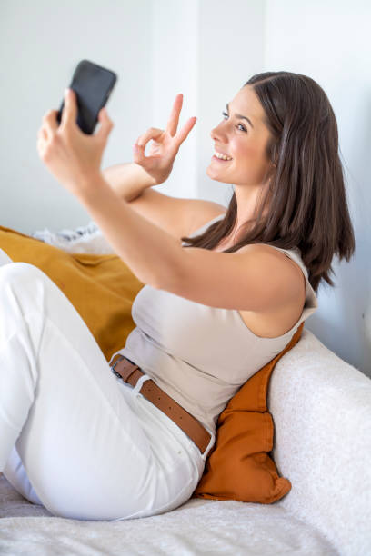 istock Taking a Fun Selfie While Relaxing Comfortably at Home, Making a Peace Sign for a Lighthearted Moment 2173398976