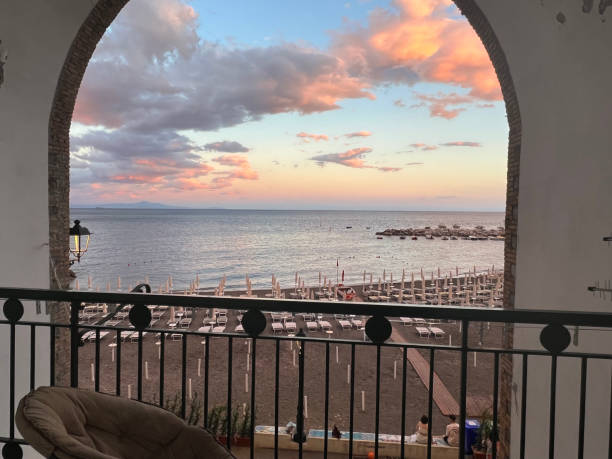 A look through an archway on a balcony overlooking sunset over the Mediterranean  with a chair overlooking a beach.