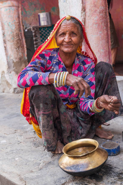 Devnagar, Ajmer, Rajasthan, India. November 8, 2022. Senior woman squatting on a sidewalk.