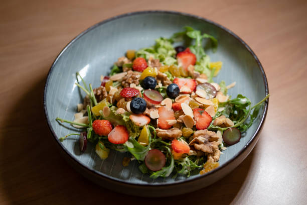 Mixed fruit salad with assorted nuts served on a plate on a wooden table. Eat clean concept.