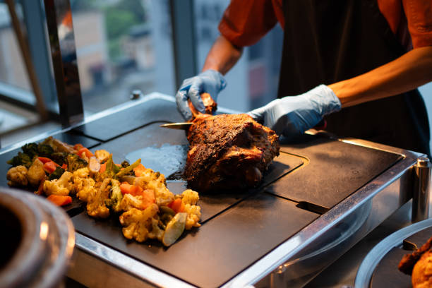 Catering chef with gloved hand slicing a lamb leg. Buffet concept.