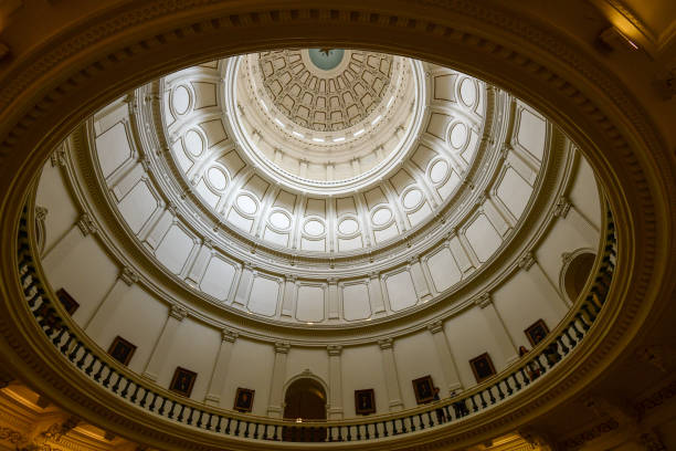 A stunning view of the Texas State Capitol in Austin, Texas, against a bright blue sky. The historic granite structure, completed in 1888, serves as the seat of government for the state of Texas. The prominent dome, adorned with the Goddess of Liberty statue, stands as a symbol of Texas pride and governance. A vintage-style street lamp in the foreground adds to the architectural charm of this iconic landmark.