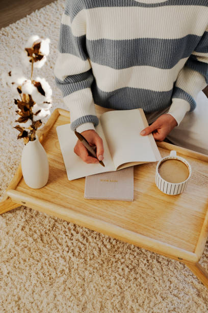 istock Cozy writing setup with a notebook, coffee, and cotton branches on a wooden tray. Perfect for creative inspiration and relaxation. Warm tones and fluffy carpet add comfort. 2173434942